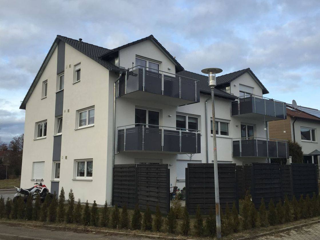 Mehrfamilienhaus mit hellem Putz, umlaufenden Balkonen und Stellplätzen